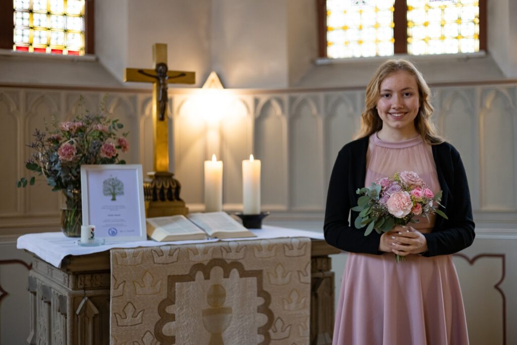 Konfirmandin steht am Alter mit ihrem Blumenstrauß