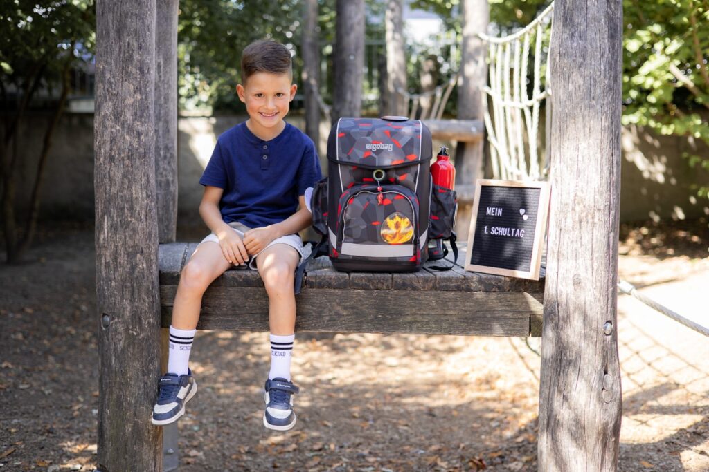 Schulkind sitzt auf Klettergerüst mit Ranzen