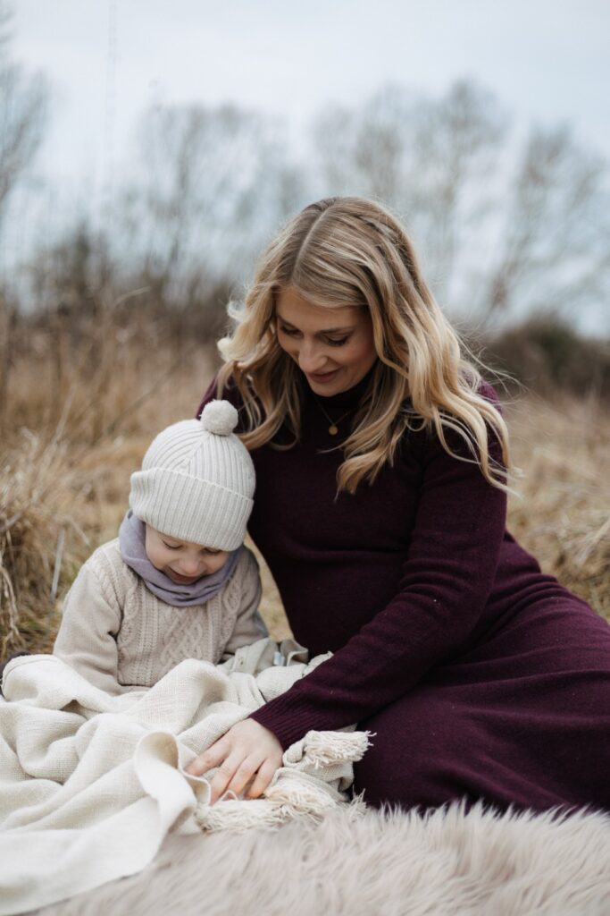 Schwangere Mama sitzt mit ihrem 3 Jährigen auf einer Decke eingekuschelt