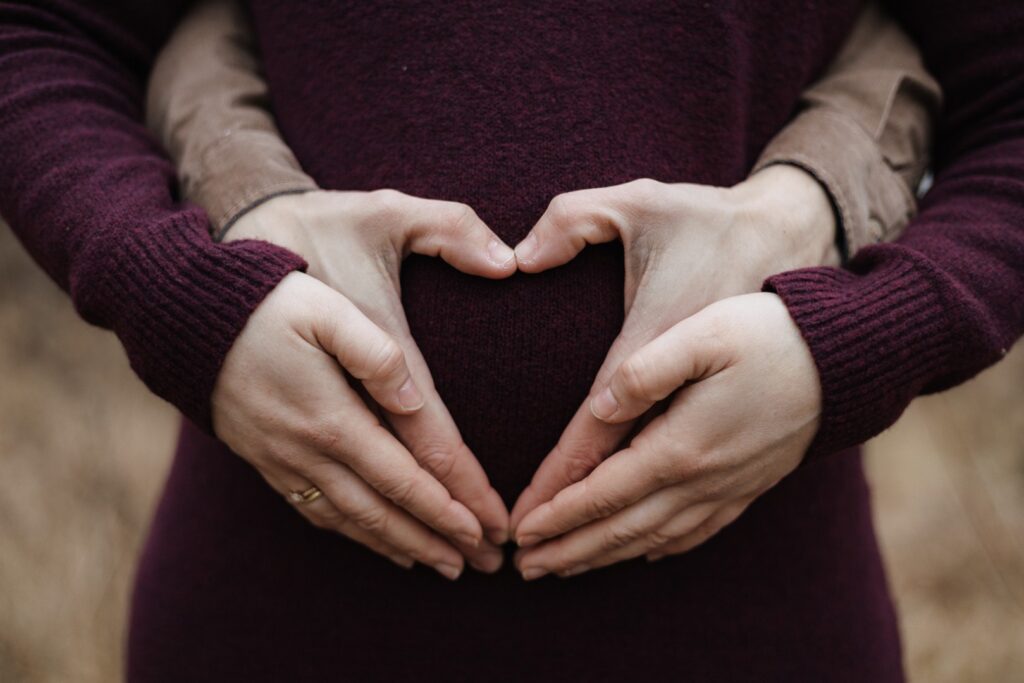 Schwangere Frau und Mann dahinter. Beide halten den Babybauch fest - Detailfoto