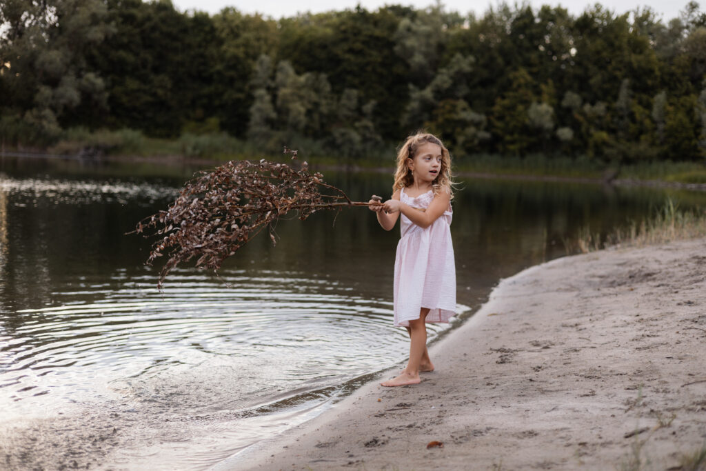 Mädchen spielt am Wasser mit einem Stock