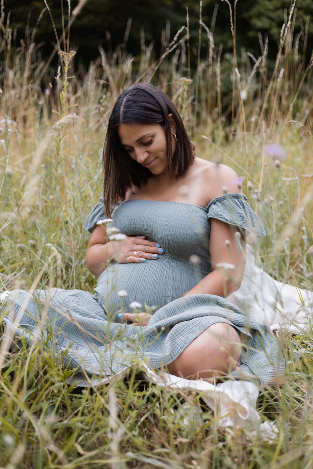 Schwangere Frau sitzt auf der Wiese und hält ihren Babybauch fest