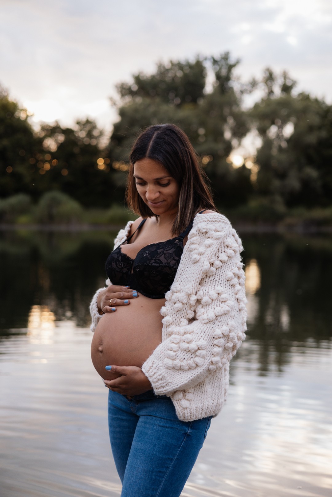 Schwangere steht am Wasser und hält ihren Babybauch fest
