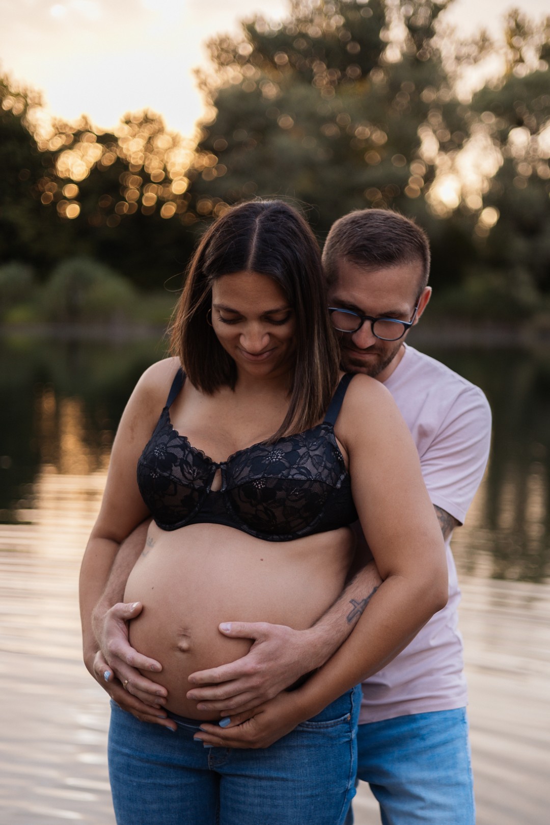 Schwangere und Ihr Mann stehen am Wasser und schauen auf den Bauch