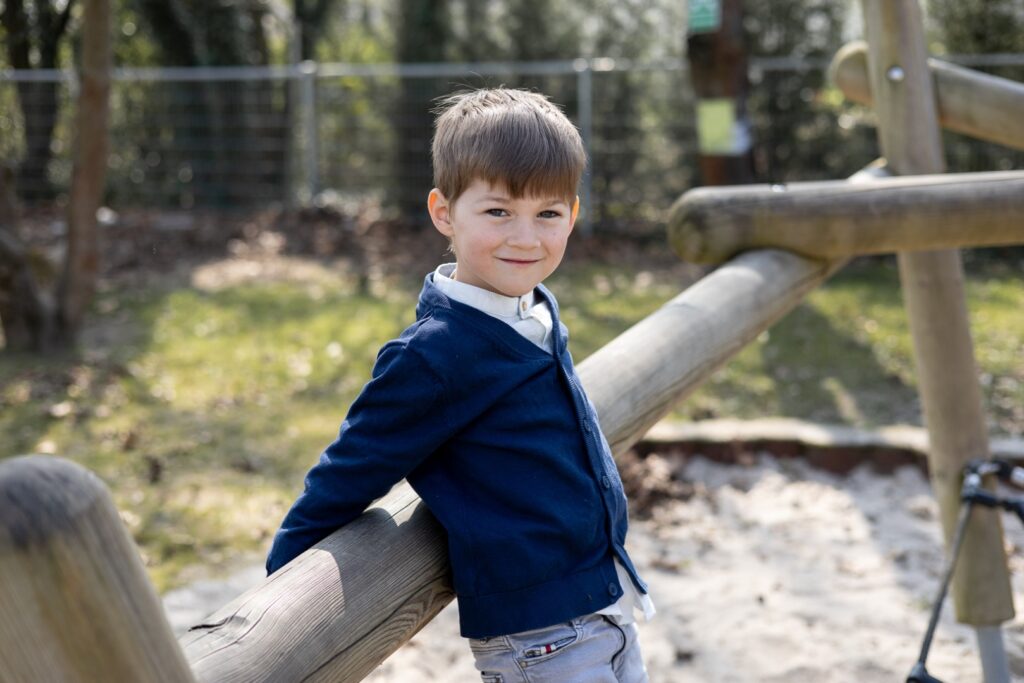 Kitakind lehnt sich am Holzbalken auf Klettergerüst an