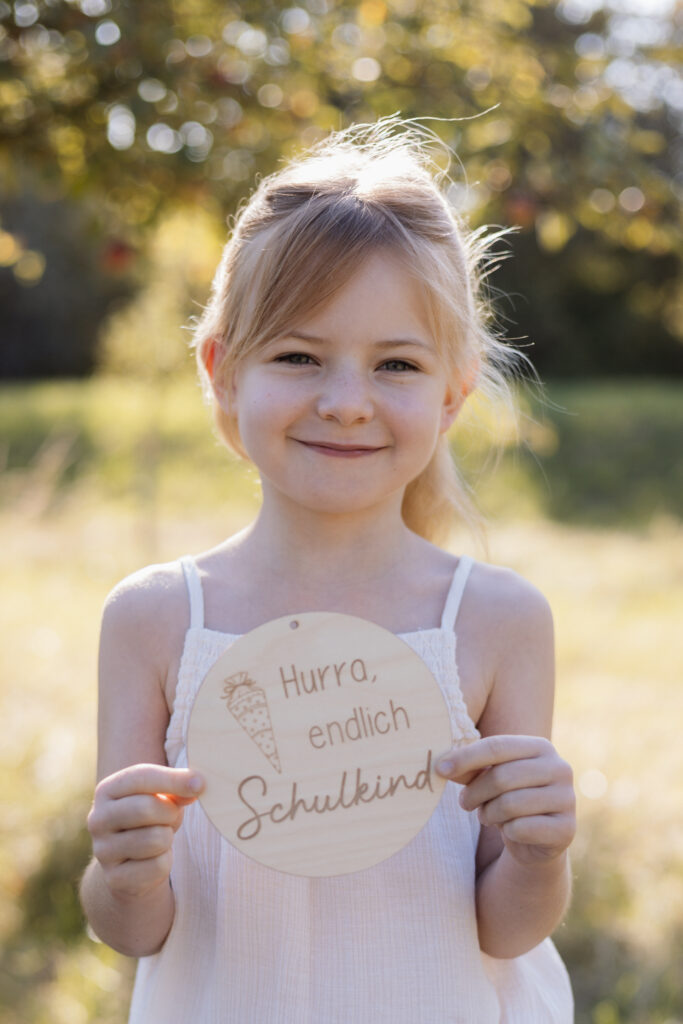 Schulmädchen hält eine Holztafel in die Kamera mit Aufschrift Hurra Endlich Schulkind