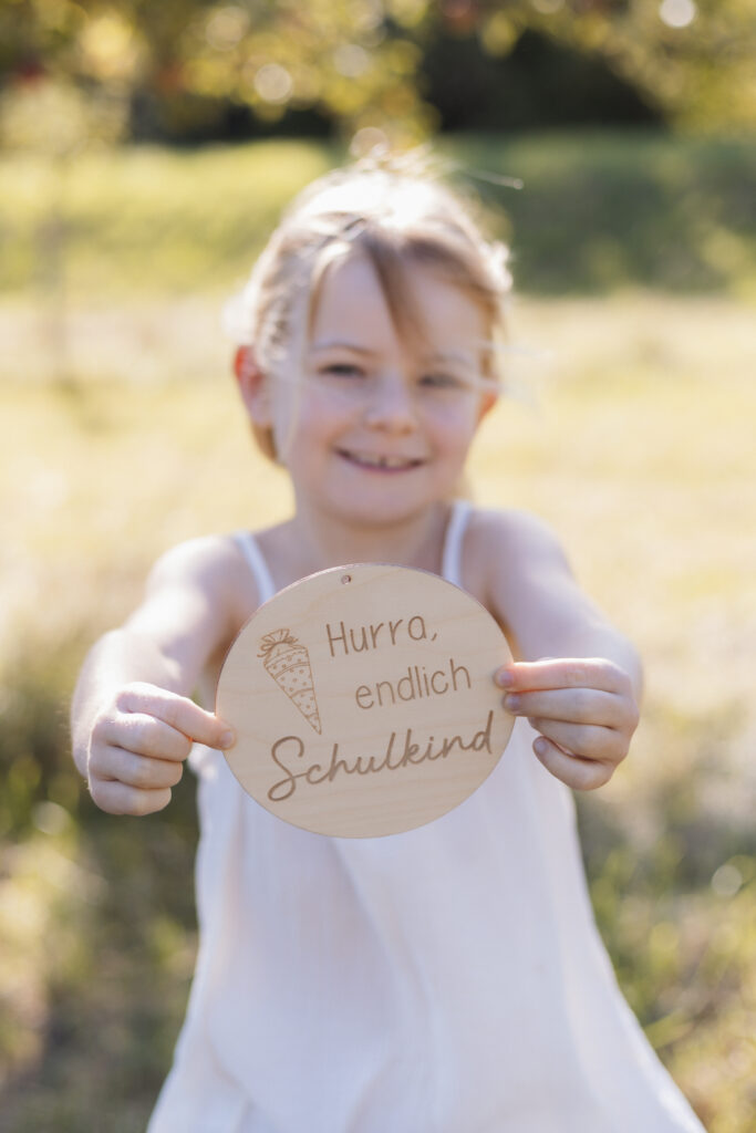 Schulmädchen hält eine Holztafel in die Kamera mit Aufschrift Hurra Endlich Schulkind