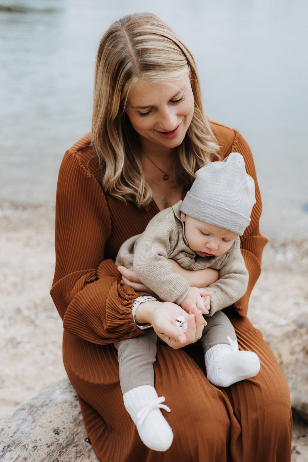 Mama und ihr Baby sitzen am Strand und bestaunen Muscheln