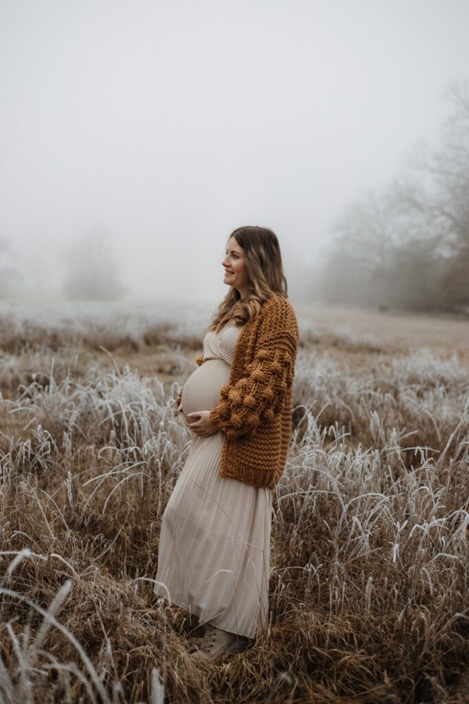 Werdende Mama schaut in die Stille des Winters und hält ihren Babybauch fest