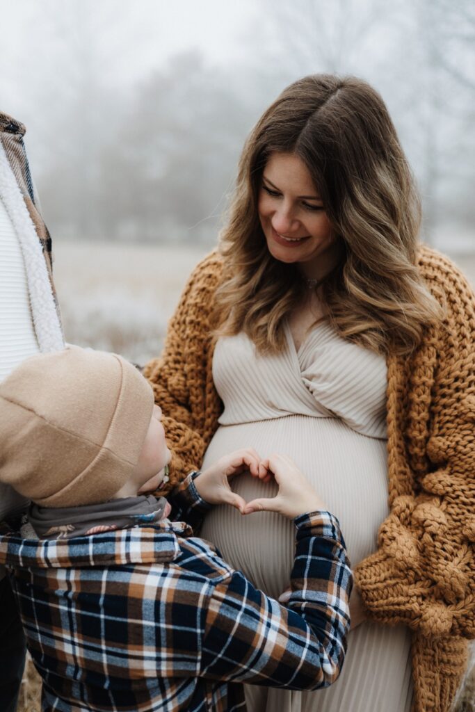 Sohn hält ein Herz auf Mamas Babybauch