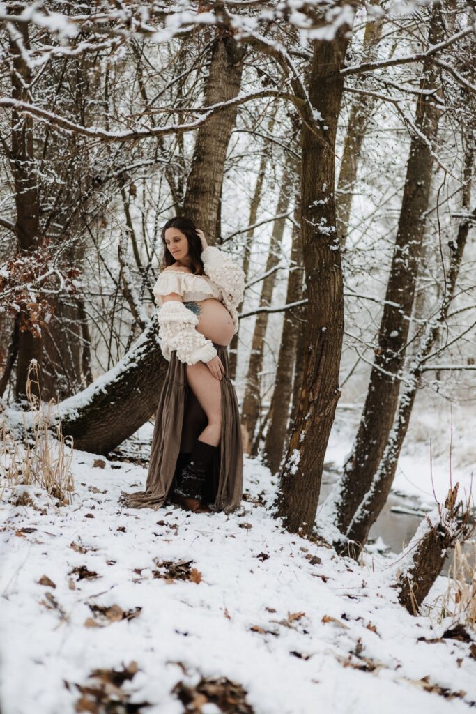 Schwangere Frau steht im Wald mit Schnee und fährt sich durch die Haare