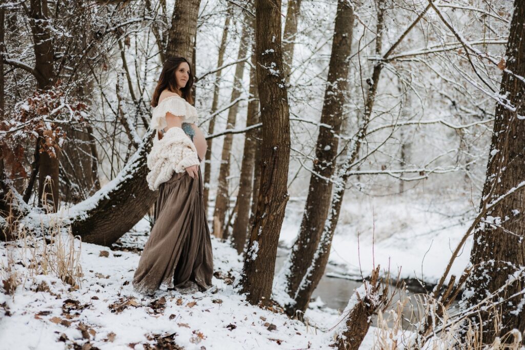 Schwangere Frau steht im Wald mit Schnee und schaut in die Ferne