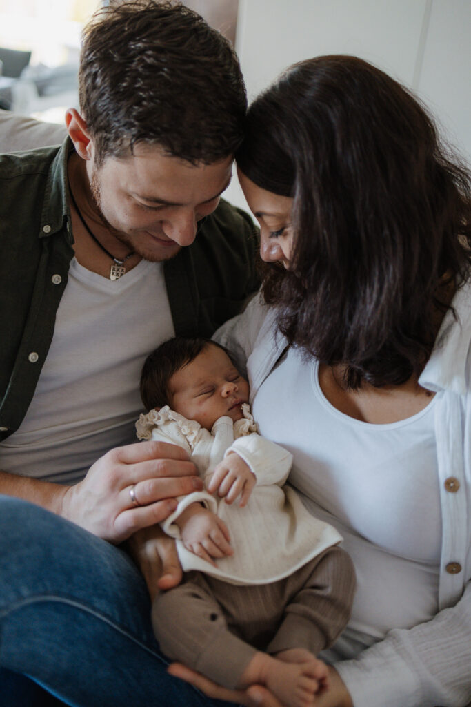 Eltern sitzen auf der Couch und halten ihr Baby im Arm
