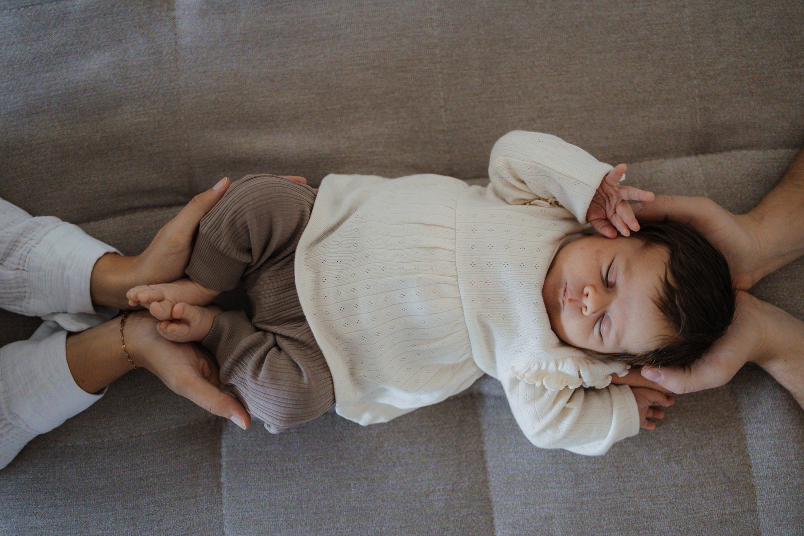 Eltern halten den Kopf und die Füße ihres Babys. Baby liegt auf der Couch