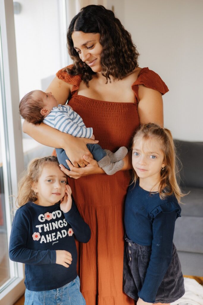 Mama hält ihr Baby im Arm, die beiden großen Schwestern stehen dicht daneben