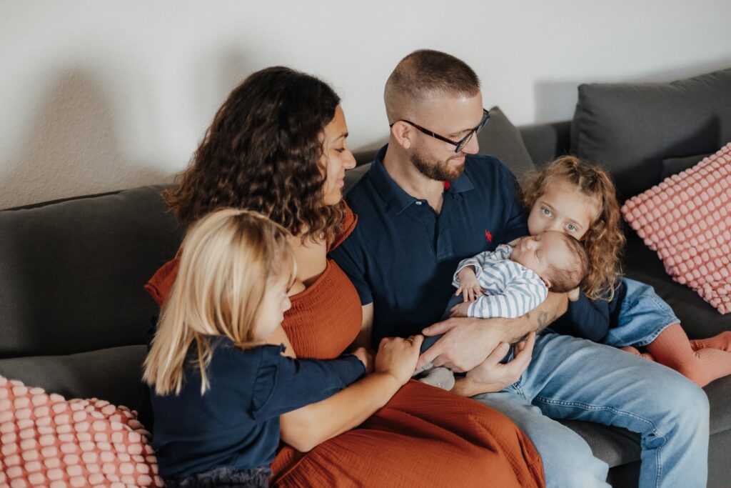 5köpfige Familie auf der Couch mit Baby im Arm vom Papa