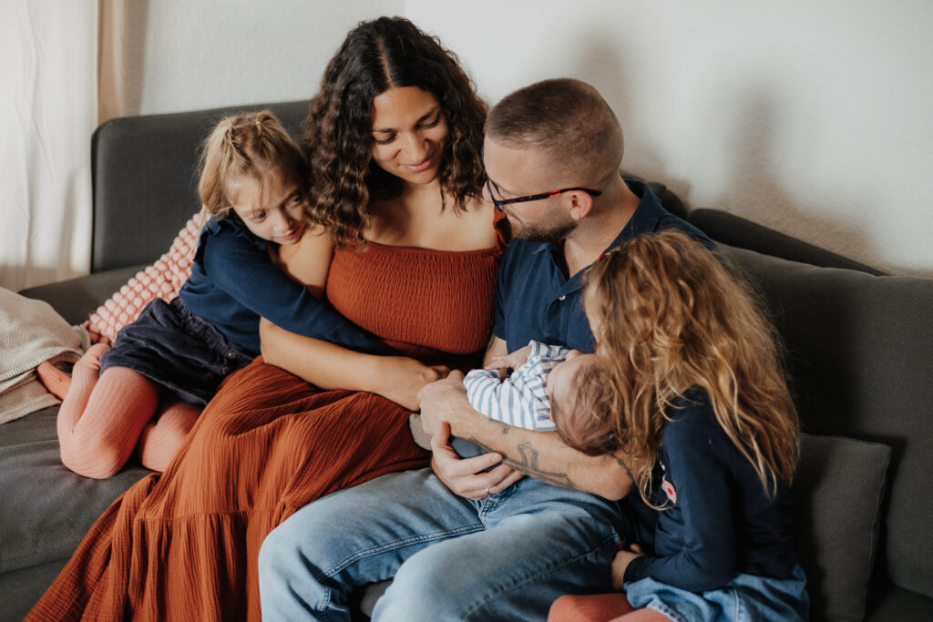 5köpfige Familie auf der Couch mit Baby im Arm vom Papa