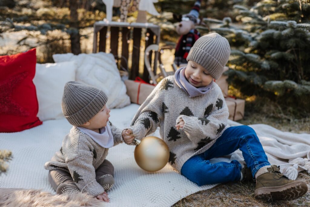 Zwei Brüder sitzen im Tannenwald auf einer Decke und spielen mit einer Christbaumkugel