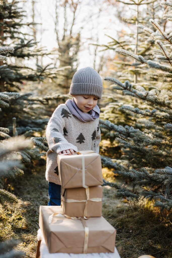 Junge schaut sich Geschenkestapel im Tannenwald an